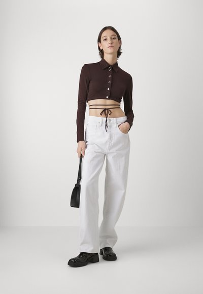 Brown cropped long-sleeve top with buttons, paired with white wide-leg trousers and black glossy shoes. Black handbag accentuates look.