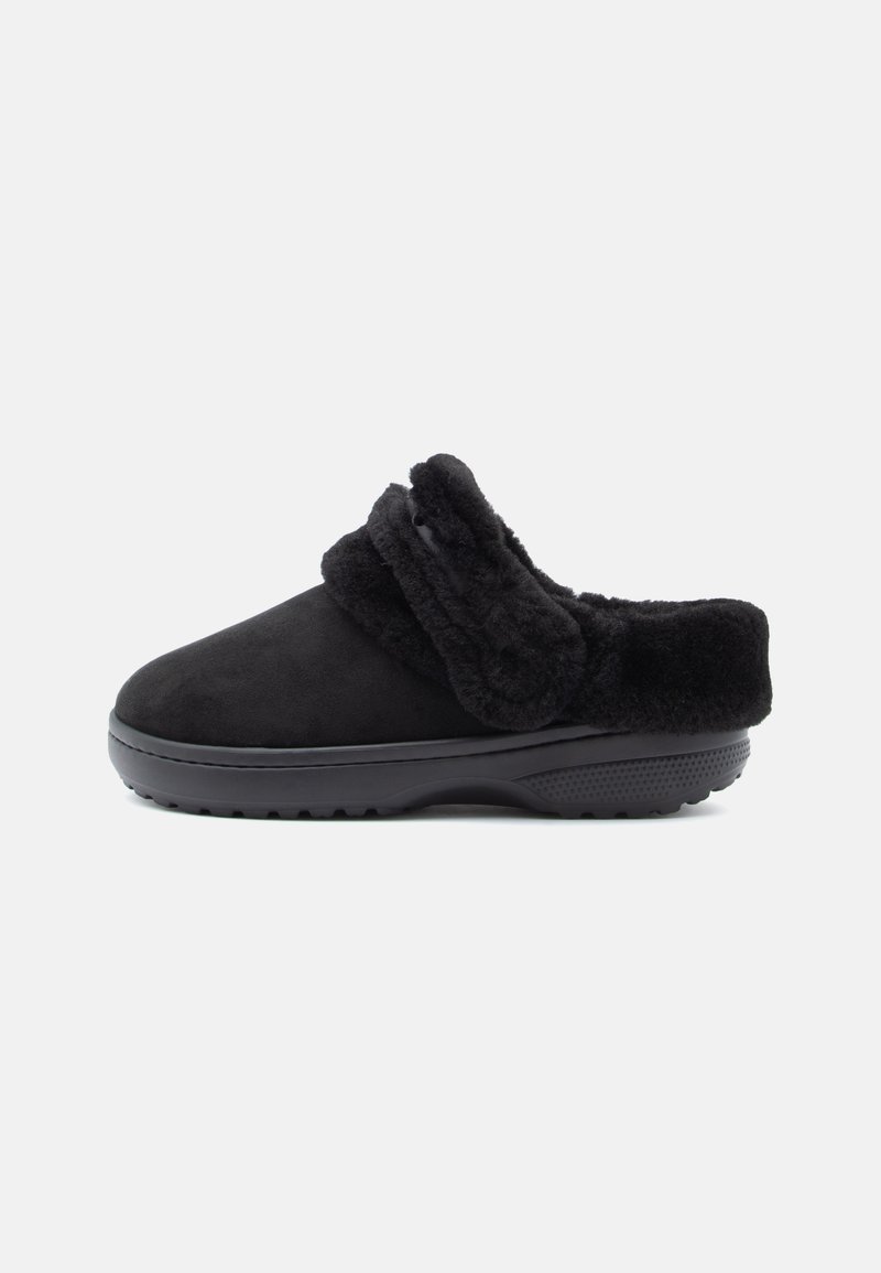 Fekete slip-on papucs vastag műszőrme béléssel és állítható pánttal a tetején, tartós texturált gumi talppal.