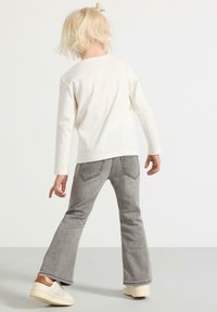 Vit långärmad skjorta kombinerad med grå utsvängda jeans. Jeans har bakfickor och minimal detaljering. Skorna är ljusa och avslappnade.