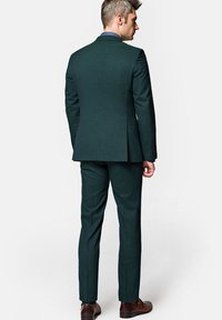 Ciemnozielony, dopasowany garnitur, teksturowana tkanina, slim fit, marynarka jednorzędowa z dwoma guzikami, pasujące spodnie, brązowe skórzane buty.