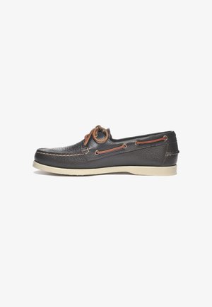 Zapato tipo bote de cuero negro con superficie texturizada, suela de goma color crema, cordones marrones pasados por los ojetes y detalles de costura en contraste.