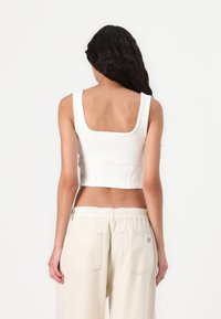 Hvit ribbet croptopp med bred firkantet hals og tykke stropper, paret med lys beige bukser med elastisk midje og baklommer.