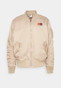 Beige Bomberjacke, satinierte Oberfläche, Reißverschluss, gerippte Bündchen und Saum, seitliche Taschen, linker Brustpatch mit horizontalen Streifen und Emblem.
