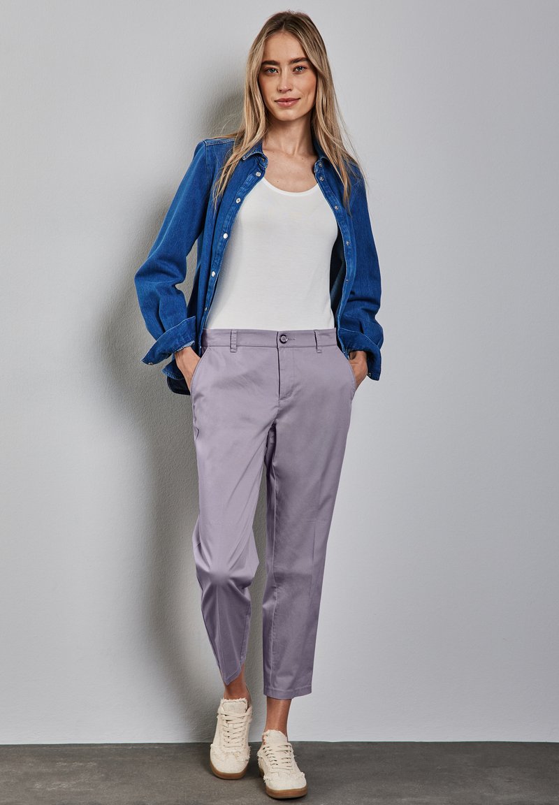 Lila byxor med slim fit, tillsammans med en vit linne och en blå jeansskjorta, bärs med krämfärgade sneakers. Slät tygtextur.