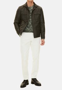 Dark green quilted jacket with two chest pockets, worn over a textured green sweater, paired with white pants and black shoes.