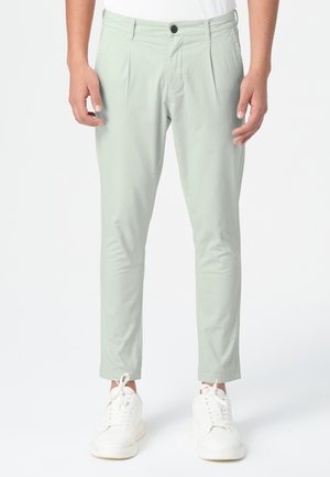 Pantalons slim-fit de couleur vert clair, avec une taille plate, des poches latérales et une taille élastique, associés à des baskets blanches. Texture de tissu lisse.