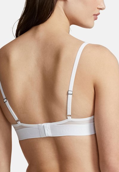 Bílý bralette s nastavitelnými ramínky, páskem s logem a hladkou texturou. Pohled zezadu odhaluje minimalistický design.