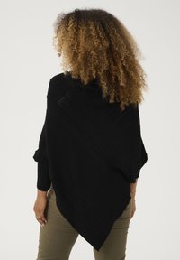 Poncho in maglia nera con colletto alto, caratterizzato da motivi a coste diagonali e un orlo asimmetrico, che scivola sul corpo.