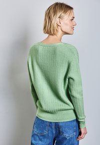 Maglione verde a maglia con una vestibilità ampia, texture a coste e maniche lunghe. Abbinato a jeans a vita alta di colore azzurro chiaro.