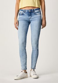 Vaqueros skinny de un azul claro deslavado, diseño de cinco bolsillos, con cierre de cremallera y botón, combinados con zapatillas blancas. Textura de denim suave.
