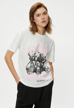 Witte katoenen t-shirt met een grafisch ontwerp van teddyberen in zwart-wit, met een roze tekstoverlay waarin staat "AMORE". Losse pasvorm, ronde hals stijl.