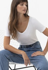 Witte V-hals T-shirt met korte mouwen, gecombineerd met high-waisted blauwe denim jeans. Soepele textuur en ontspannen pasvorm, minimalistisch ontwerp.