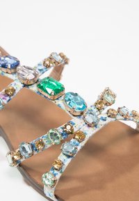 Sandales avec des brides à motif floral ornées de pierres précieuses facettées bleues, vertes et ambrées, gros plan détaillé sur la semelle avant.