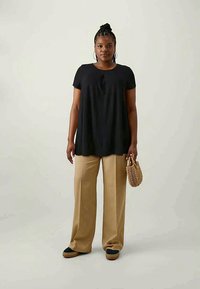 Top negro de manga corta con escote redondo, de corte holgado, combinado con pantalones beige holgados y zapatos de plataforma. Lleva un bolso de mimbre.