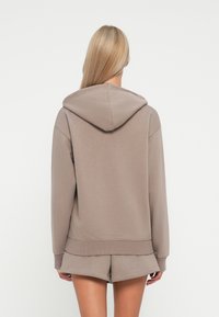 Brown hoodie with a relaxed fit, features a hood, ribbed cuffs, and hem. Paired with matching shorts, showcasing a soft texture.