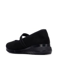 Zapatos de ante negro tipo slip-on con punta redondeada, tiras elásticas visibles y suela de goma texturizada en negro. Diseño elegante y de perfil bajo.