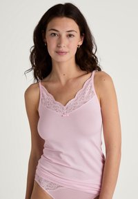 Light pink camisole featuring a floral lace neckline and a small pink bow accent, with thin straps and a soft, smooth texture.