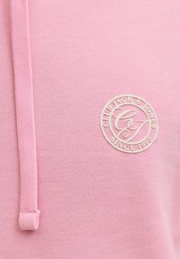 Vaaleanpunainen puuvillainen huppari, jossa on teksturoitu kiristysnaru. Hupussa on vaalea pyöreä logo, jossa lukee "CLUB BLACK & JONES" ja "SINCE 1990".