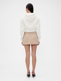 Hvit cropped hettegenser med hette, kombinert med et beige A-linjekjole. Modellen bruker svarte hælsandaler, som viser en enkel silhuett.