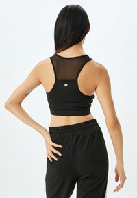 Svart sport-BH med en mesh-panel på baksidan, racerback-design och en liten logga i mitten. Matchas med svarta träningbyxor.