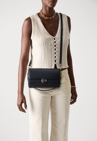 Sac bandoulière en cuir marine avec une forme structurée, une fermeture à rabat avant avec une boucle en or et une sangle réglable.