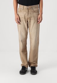 Beige denim jeans met een rechte pasvorm. Voorzien van vijf zakken, een metalen knoopsluiting en subtiele vervaging voor textuur. Draagt met zwarte sneakers.