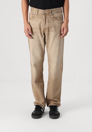 Beige denim jeans met een rechte pasvorm. Voorzien van vijf zakken, een metalen knoopsluiting en subtiele vervaging voor textuur. Draagt met zwarte sneakers.