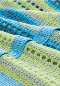 Stickad tyg i blått och grönt med texturerade ränder. Har knäppningar med knappar och ett öppet vävmönster för andningsförmåga.