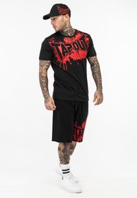 Conjunto de camiseta negra y pantalones cortos con estampado gráfico rojo "TAPOUT", mangas cortas, ajuste relajado, material de algodón y gorra negra a juego.