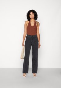 Bodysuit castanho com alças, combinado com jeans de perna larga pretos de cintura alta. O modelo segura uma pequena mala bege, usando sandálias brancas com tiras.
