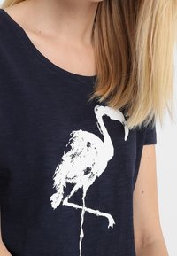 Granatowa koszulka z krótkim rękawem z białą, stylizowaną grafiką żurawia na przodzie; wykonana z miękkiego materiału, z okrągłym dekoltem.