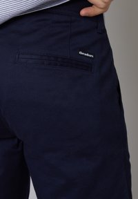 Pantalon marine au toucher lisse, doté d'une poche arrière et d'une étiquette de marque noire. Design simple avec une coupe droite.