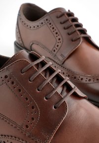 Brown leather lace-up shoes with perforated detailing, rounded toe, smooth texture, and contrasting stitching along the edges.