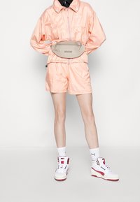 Růžový lesklý teplákový komplet s elastickým pasem a šňůrkou, doplněný bílými teniskami s vysokou podešví a červenými akcenty.