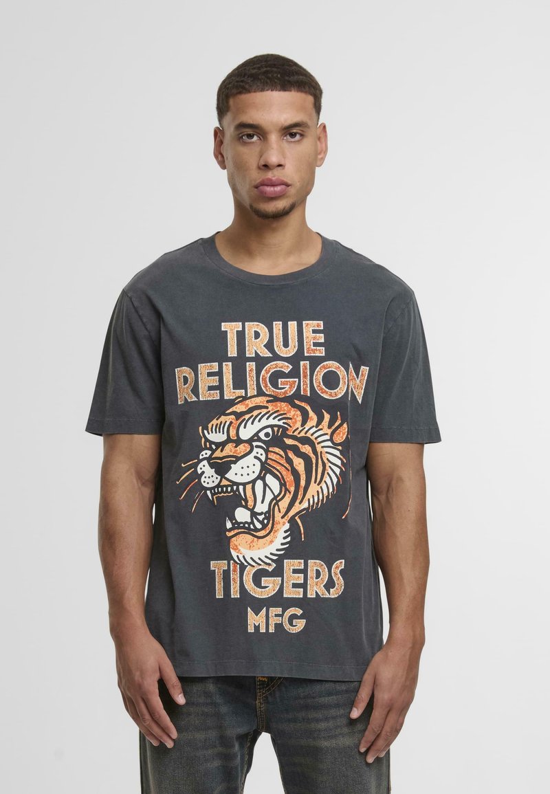 Kokogai pelēks kokvilnas t-krekls ar tīģera grafiku oranžā un baltā krāsā, zem kura ir uzraksts "TRUE RELIGION TIGERS MFG". Īsās piedurknes.