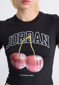 Black short-sleeve t-shirt featuring "JORDAN" text. Graphic of two basketballs resembling cherries, with "Established 1984" at the hem.