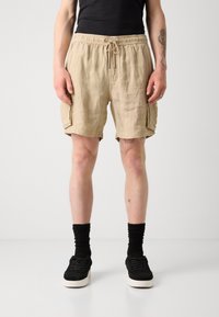 Shorts beige in lino con vita elasticizzata, cordino e tasche laterali. Indossati con sneaker nere e calzini. Tessuto semplice senza motivi.