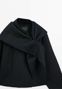 Black coat with oversized draped collar folded over the front, displayed on a white background.