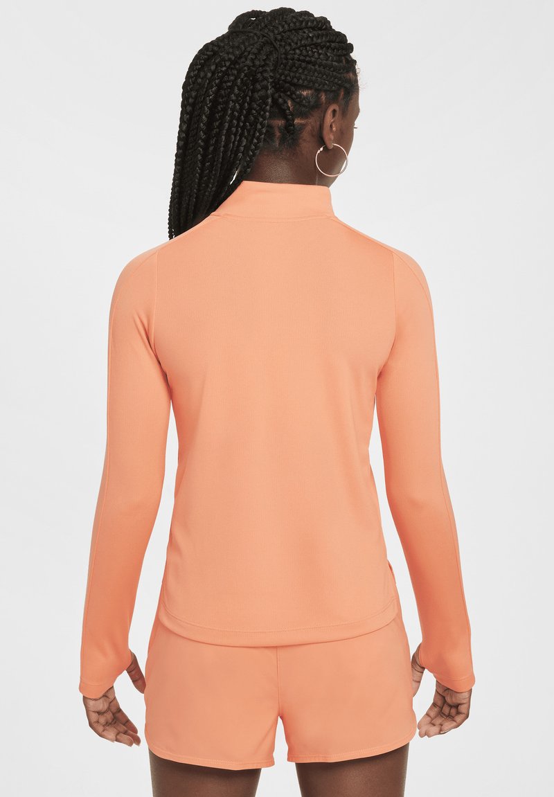 Langärmliges Sportoberteil und Shorts aus leichtem orangefarbenem Stoff, mit hohem Kragen, glatter Textur und taillierter Passform.