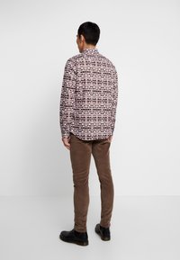 Hemden met lange mouwen bedrukt met een kleurrijk geometrisch patroon, met kraag, gecombineerd met een bruine corduroy broek en zwarte schoenen.