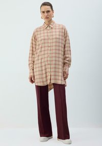 Chemise à boutons en tartan rose et jaune, avec manches longues et ourlet asymétrique, associée à un pantalon taille haute bordeaux.