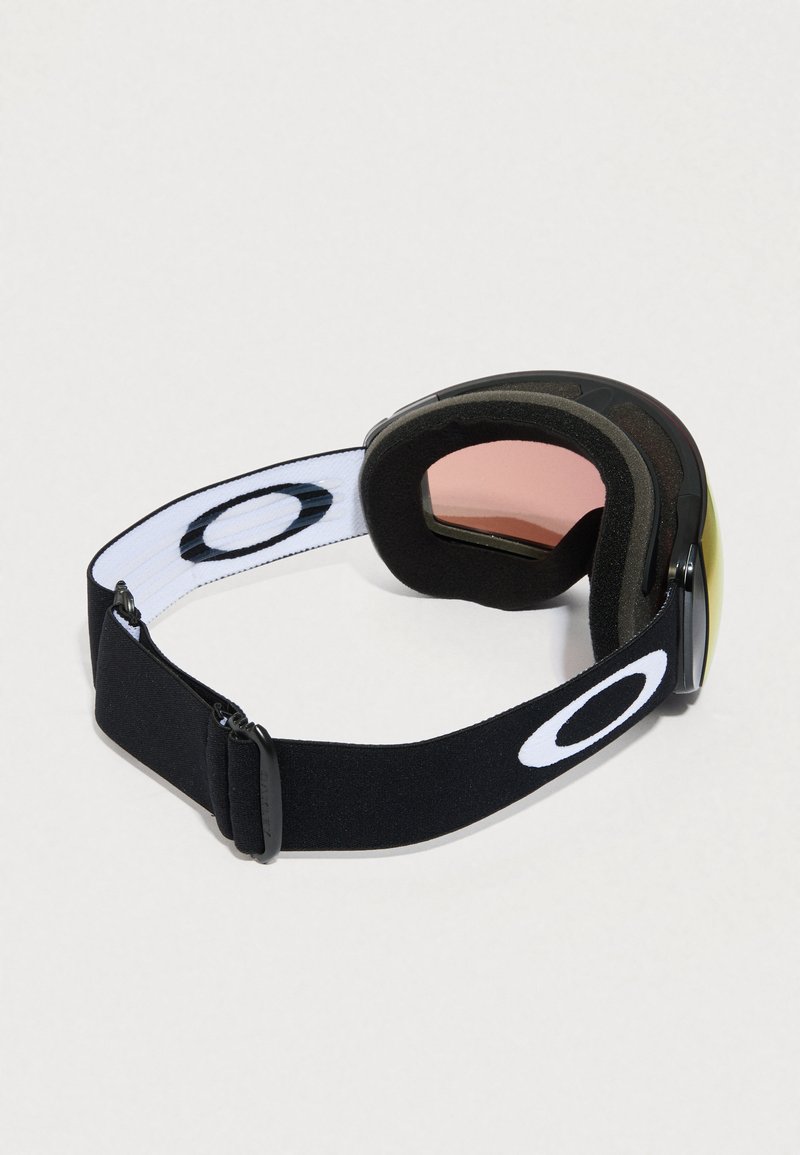 Lunettes de ski Oakley en noir et blanc avec des verres teintés rose et un rembourrage en mousse, vues de l'arrière et de côté sur un fond clair.