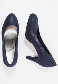 Zapatos de tacón alto en azul marino con superficie texturizada, punta redondeada y plantilla de metal plateado. Tacones bajos y forro suave.
