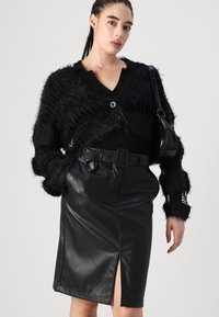 Μαύρο φ fuzzy κάρντιγκαν με V λαιμόκοψη και κουμπιά, συνδυασμένο με εφαρμοστό μαύρο δερμάτινο φούστα με εμπρός σχισμή και ζωνάκι στη μέση.