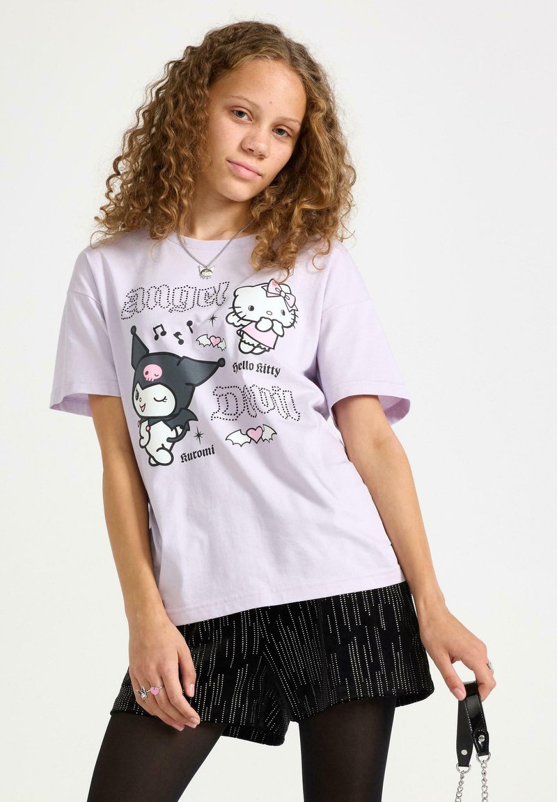 Jasnofioletowa bawełniana koszulka z nadrukiem Hello Kitty i Kuromi z nietoperzami, w zestawie z czarnymi szortami z metalicznymi akcentami.