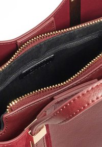 Bordeaux handtas met een soepele textuur, gouden rits en zwarte voering. Heeft een ritsvak en een platte banddetails.
