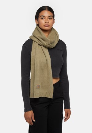 Scarf in maglia verde oliva a costine, adagiato intorno al collo, con un piccolo patch logo. La sciarpa ha una texture morbidissima e forma rettangolare.