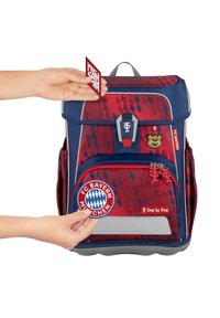 Sac à dos rouge et bleu avec des motifs géométriques, des bretelles réglables, des poches latérales et des patchs FC Bayern Munich amovibles. Texture lisse.