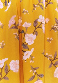 Gele stof met een bloemendessin waarop roze en witte bloemen en groene bladeren zijn afgebeeld. De textuur is zacht en licht gestructureerd.