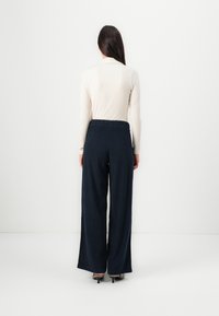 Pantaloni larghi blu notte realizzati in tessuto strutturato, dotati di una cintura elastica, abbinati a un top aderente e rigato di colore chiaro.
